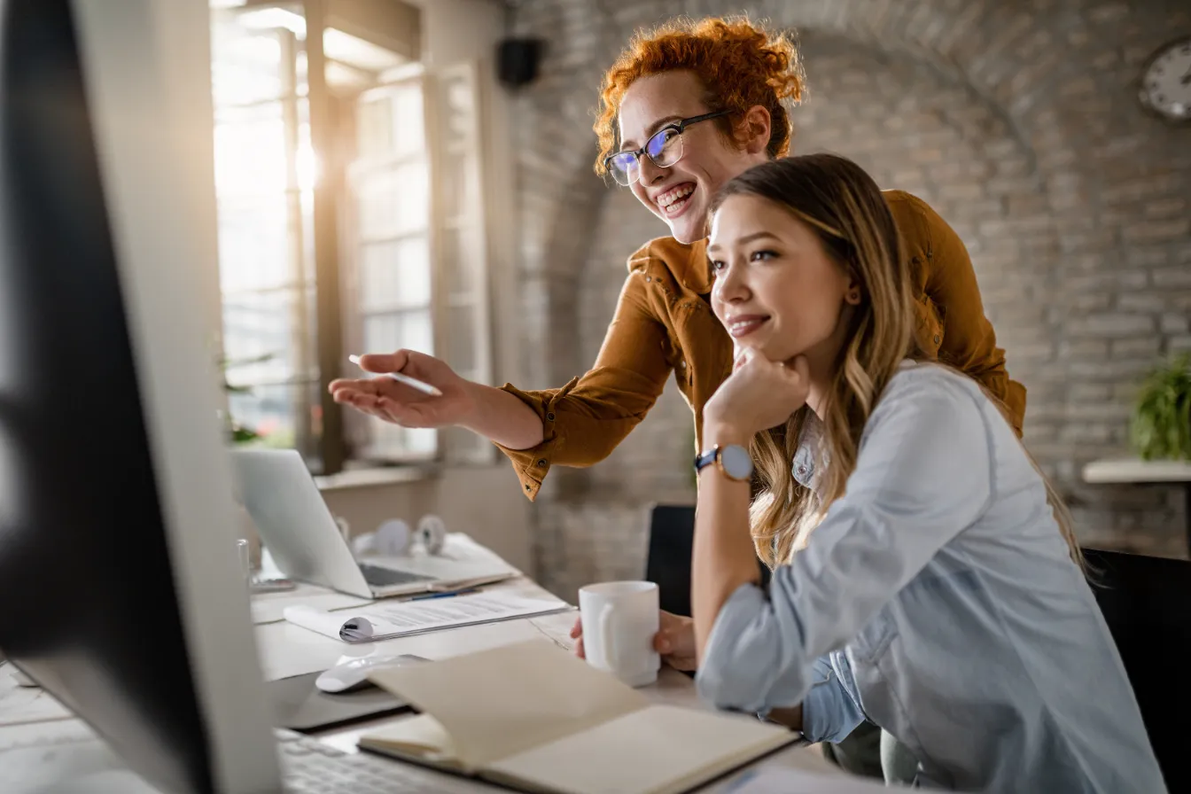 two women smile at a computer screen